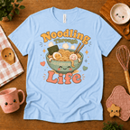 Noodling Through Life cute food graphic t-shirt cozy flat lay in baby blue.