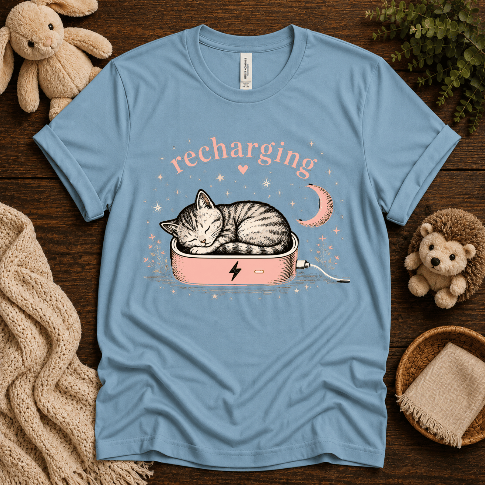 Recharging Cat cute animal graphic t-shirt cozy flat lay in baby blue.