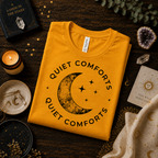 A folded mockup of Quiet Comforts black print celestial graphic t-shirt in gold.
