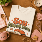 Folded mock up of Soy Happy Here graphic t-shirt in natural, surrounded by small kitchen utensils.