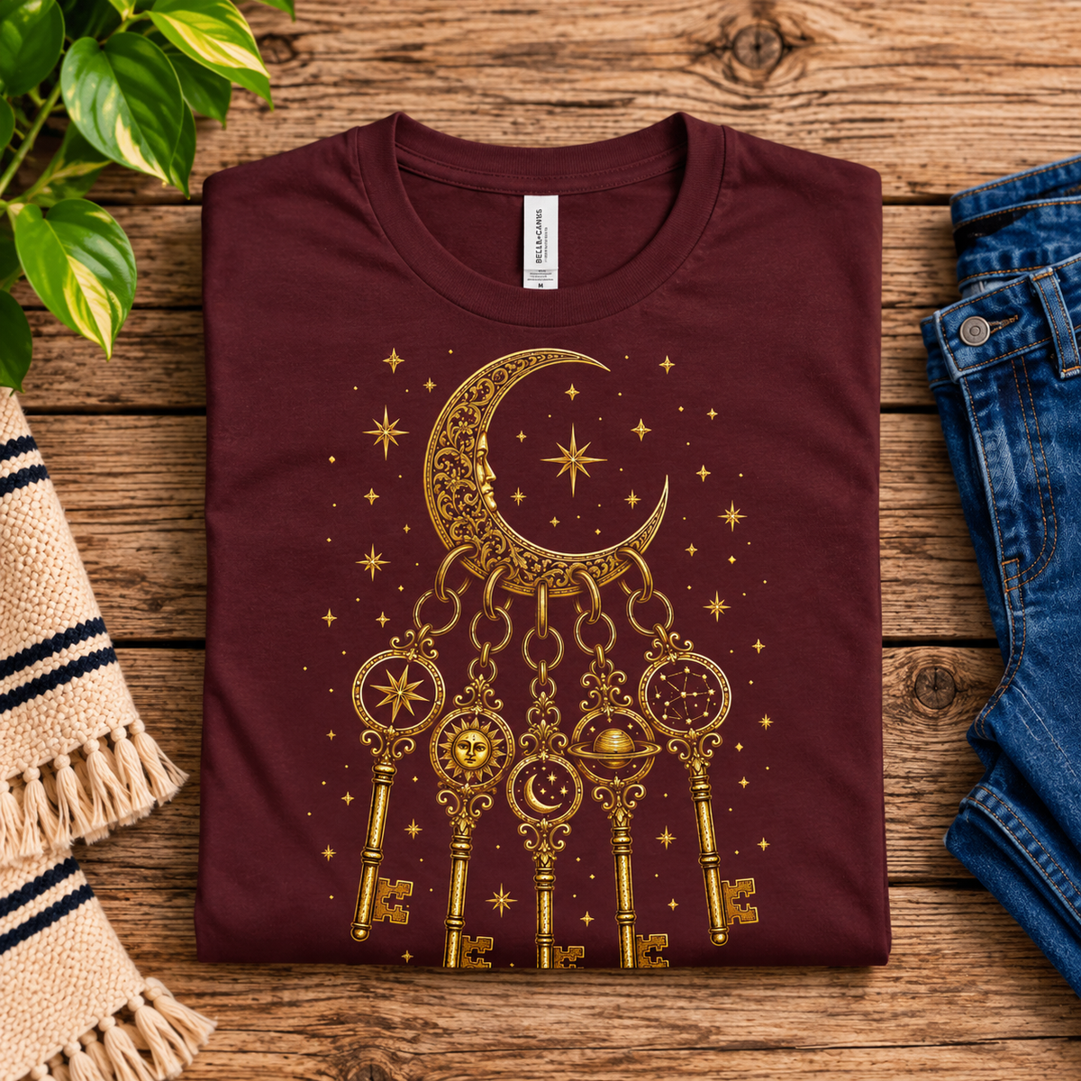 A folded mockup of Cosmic Keyring whimsical celestial graphic t-shirt in maroon.