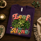 A folded mockup of Leaf Me Alone cute plant graphic t-shirt in team purple