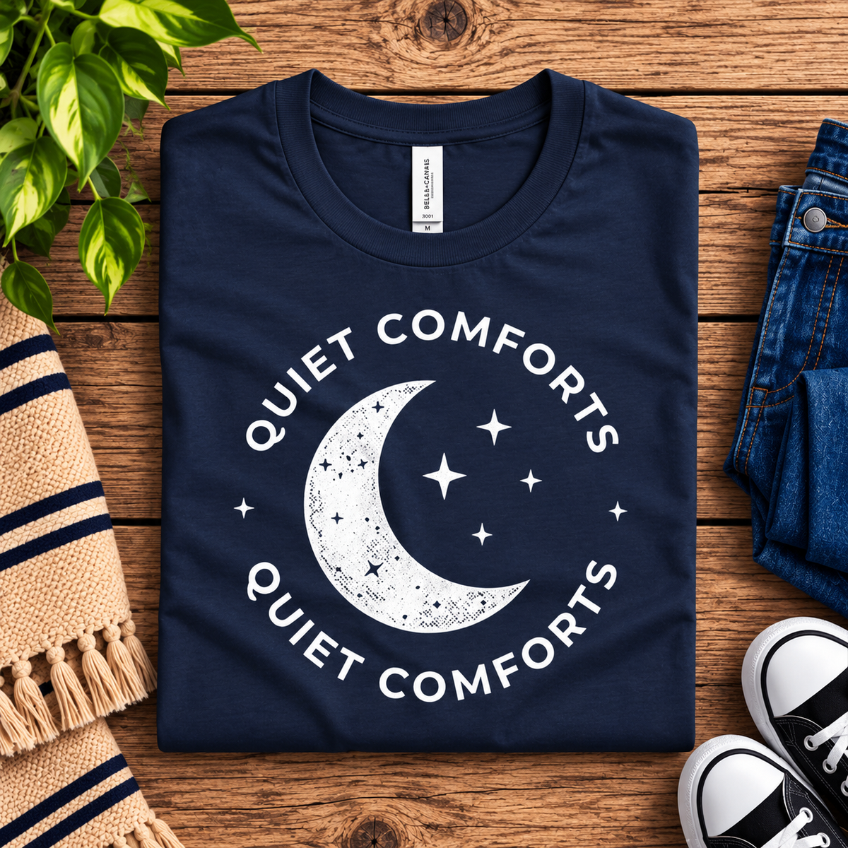 A folded mockup of Quiet Comforts celestial graphic t-shirt in deep teal.