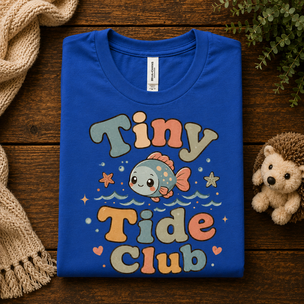 A folded mockup of Tiny Tide Club cute animal graphic t-shirt in true royal.