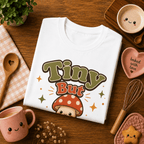 Folded mock up of Tiny But Tasty graphic t-shirt in white, surrounded by small kitchen utensils.