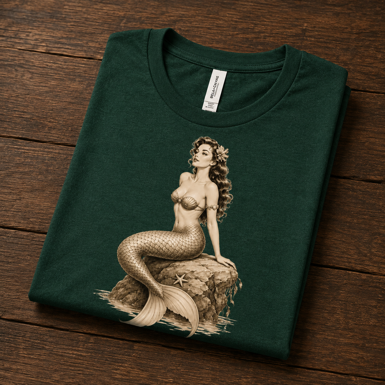 Folded mock up of Beach Mermaid graphic t-shirt in evergreen on a dark wood background.