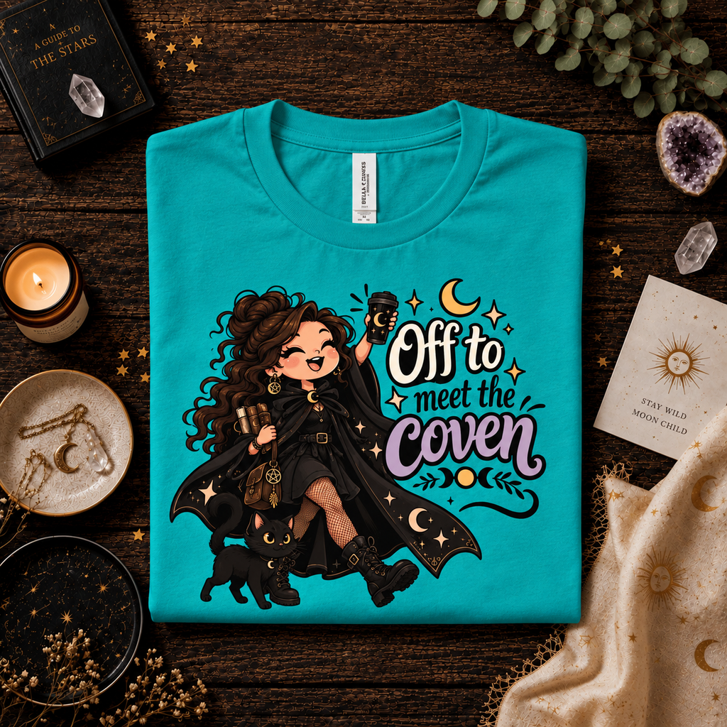 A folded mockup of Off to Meet the Coven witchy celestial graphic t-shirt in heather sea green.