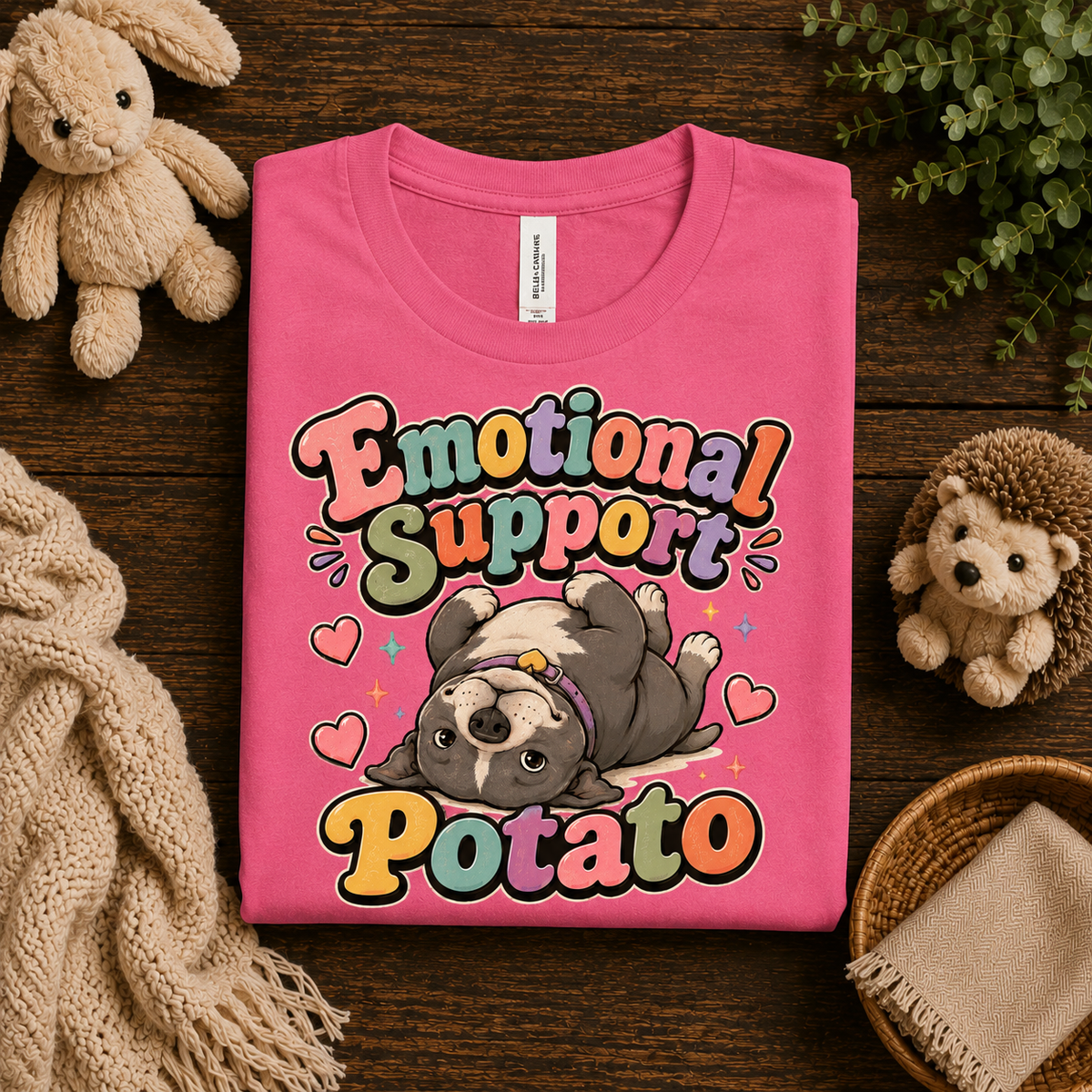 A folded mockup of Emotional Support Potato cute animal graphic t-shirt in charity pink.