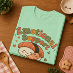 Folded mock up of Emotional Support Sushi graphic t-shirt in mint, surrounded by small kitchen utensils.