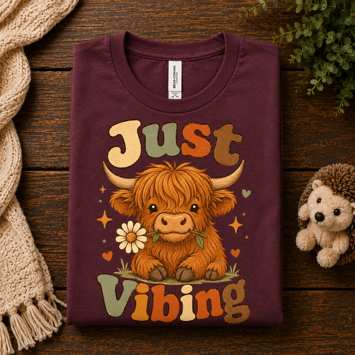 A folded mockup of Just Vibing Cow cute animal graphic t-shirt in maroon.