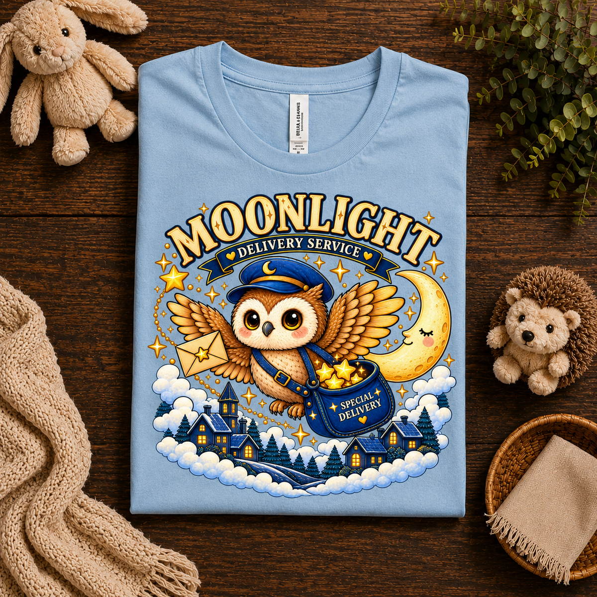A folded mockup of Moonlight Delivery cute animal graphic t-shirt in baby blue.