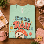 Folded mock up of I'm On A Roll graphic t-shirt in mint, surrounded by small kitchen utensils.