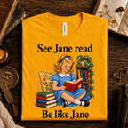 A folded mockup of See Jane Read vintage book graphic t-shirt in gold.