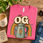 A folded mockup of The OG retro coffee graphic t-shirt in charity pink.