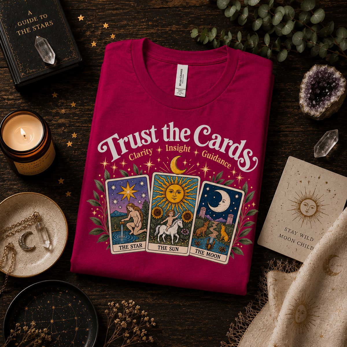 A folded mockup of Trust The Cards celestial tarot graphic t-shirt in berry.