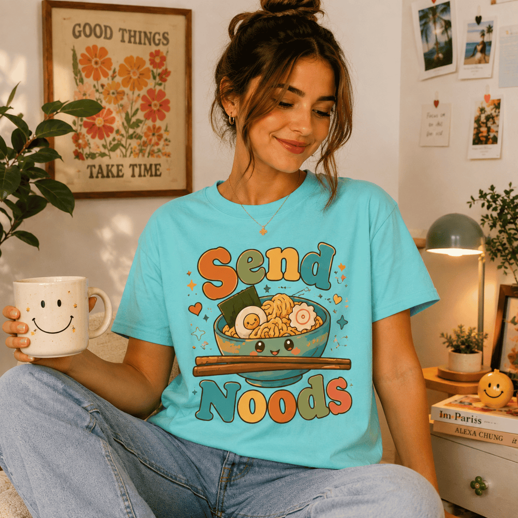 Woman wearing Send Noods graphic t-shirt in aqua sitting at a desk, taking a break with coffee.