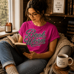 A woman wearing a berry Book Worm book lover graphic t-shirt reading a book near a window.