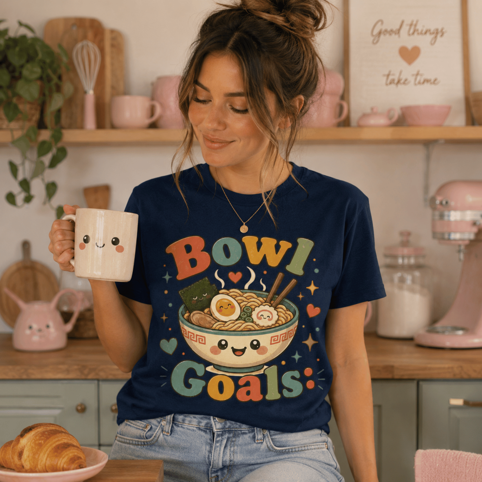 Woman wearing Bowl Goals graphic t-shirt in navy sitting on kitchen stool, drinking coffee.