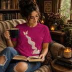 A woman wearing a charity pink Rainbow Book whimsical book graphic t-shirt reading a book.