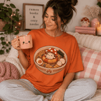 Woman wearing Mushroom Float graphic t-shirt in burnt orange sitting on couch drinking coffee.