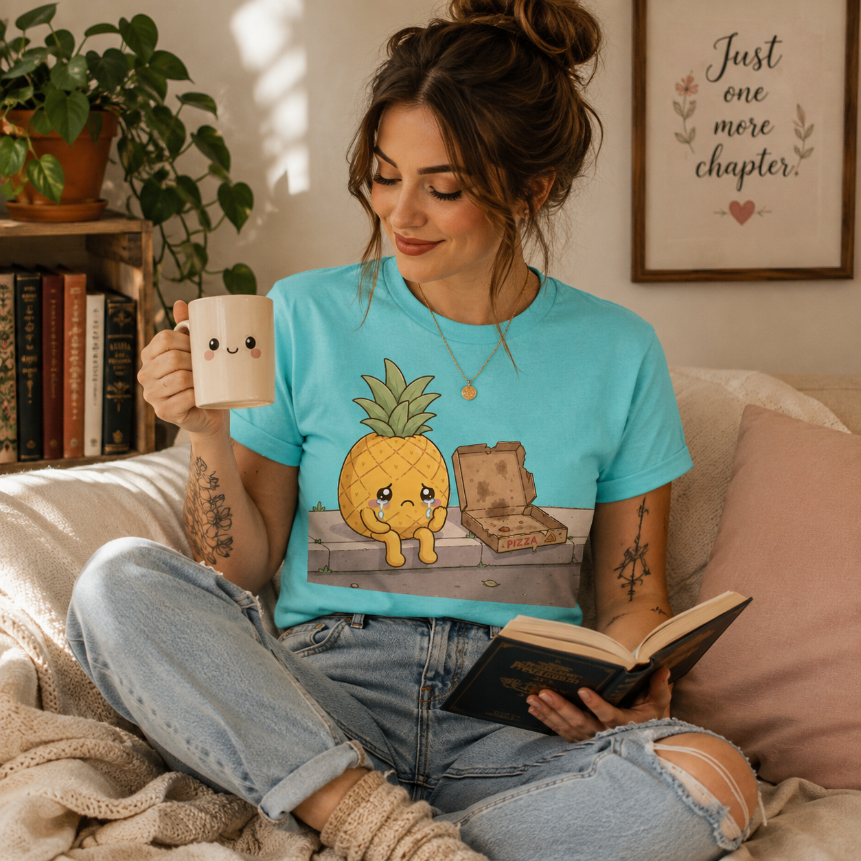 Woman wearing Pineapple Pizza graphic t-shirt in aqua sitting on a couch drinking coffee.