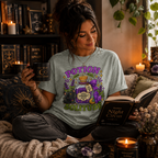 A woman wearing an athletic heather Potion Of Solitude cute witchy graphic t-shirt drinking coffee.