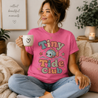 A woman wearing a charity pink Tiny Tide Club cute animal graphic t-shirt drinking coffee.