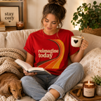 A woman wearing a red Reimagine Today inspirational introvert graphic t-shirt drinking coffee.