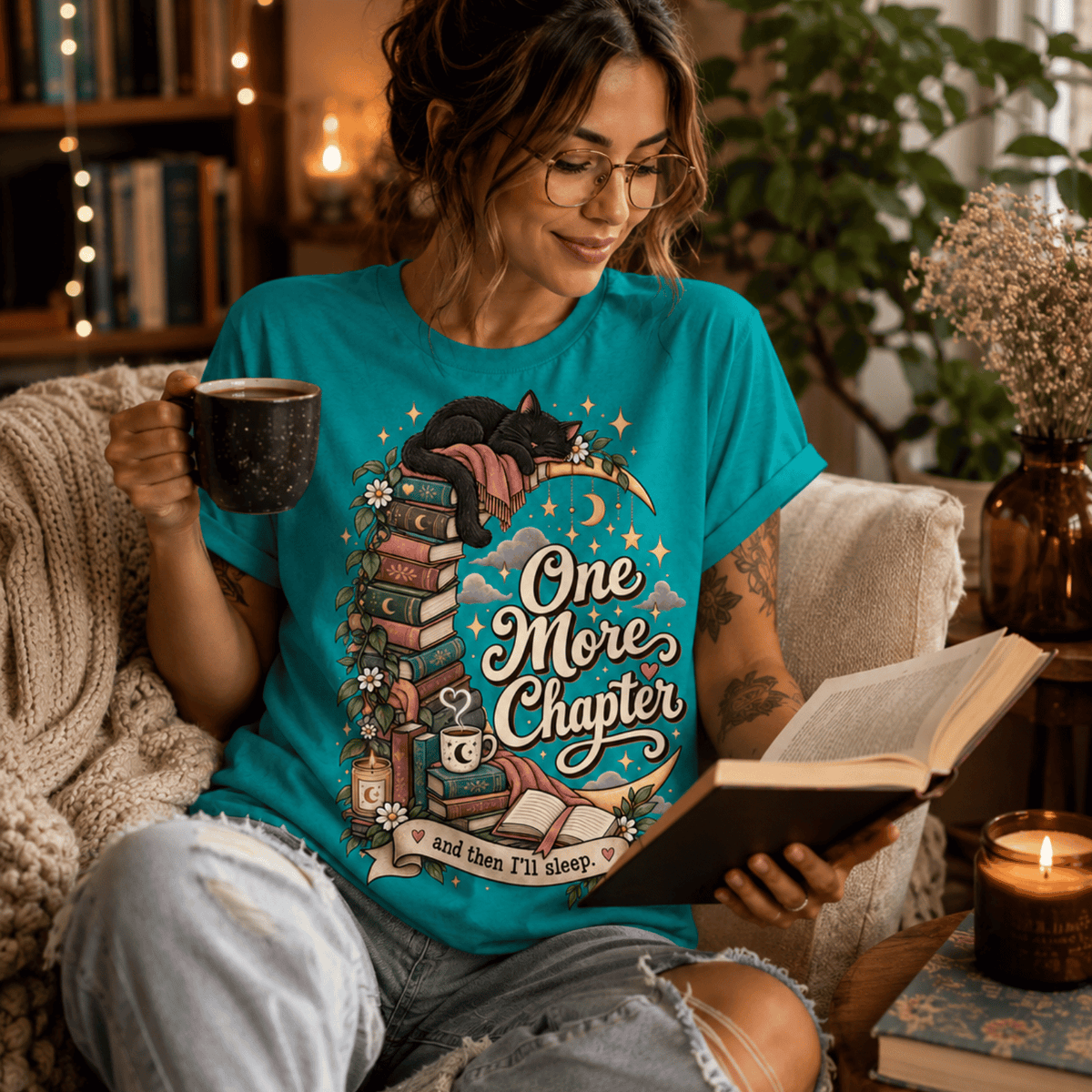 A woman wearing a heather sea green One More Chapter cute book graphic t-shirt reading a book.