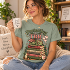 A woman wearing a Protecting My TBR cute book graphic t-shirt in sage.