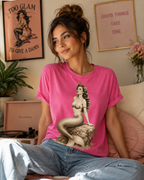 Woman wearing Beach Mermaid graphic t-shirt in charity pink in living room.
