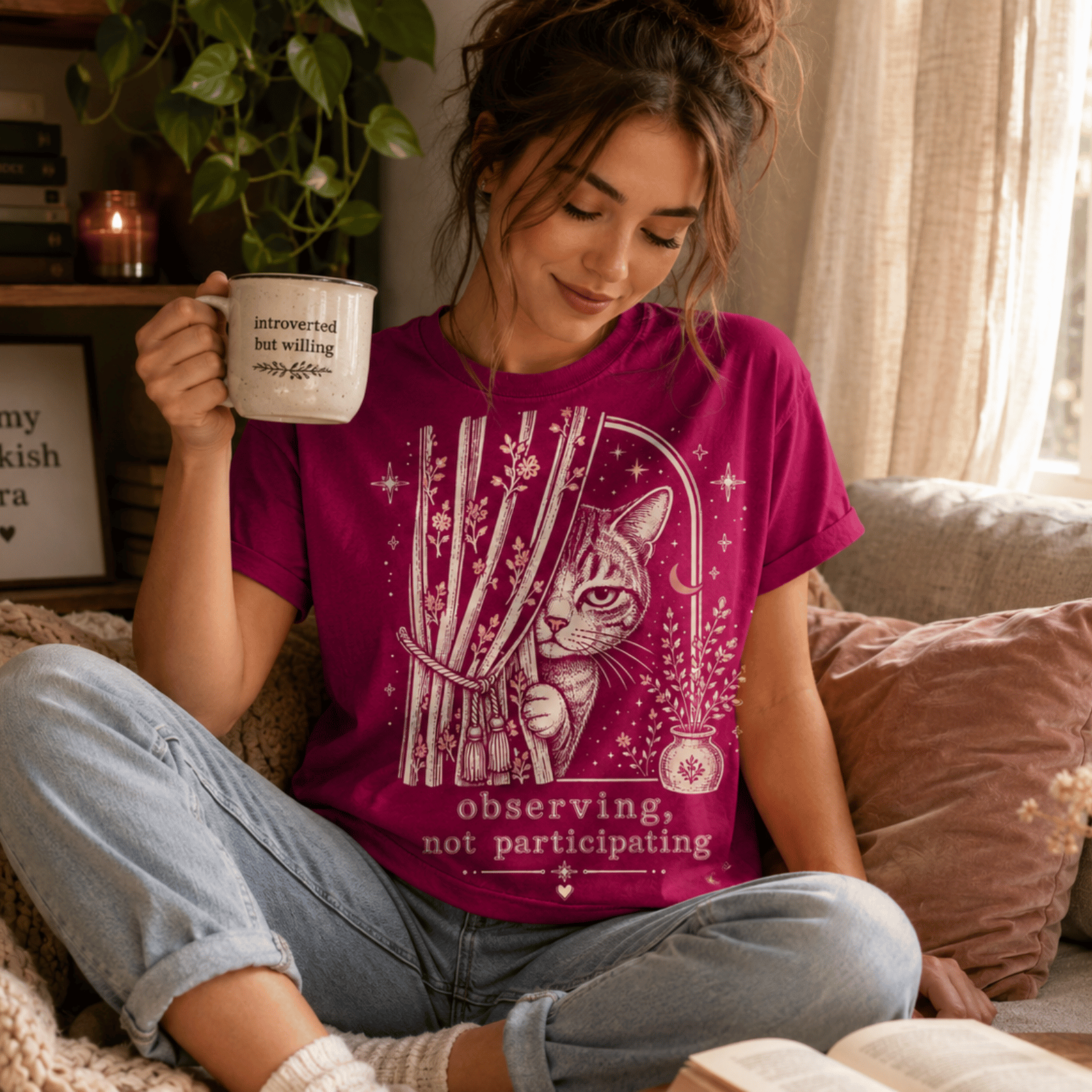 A woman wearing a berry Cat Observing graphic t-shirt drinking coffee.