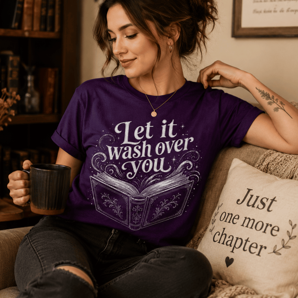 A woman wearing a team purple Let It Wash Over You whimsical book graphic t-shirt drinking coffee.