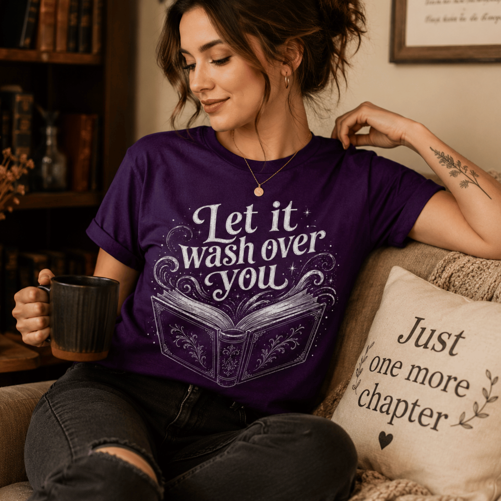 A woman wearing a team purple Let It Wash Over You whimsical book graphic t-shirt drinking coffee.
