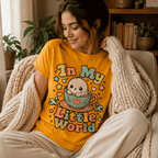 A woman wearing a gold In My Little World cute animal graphic t-shirt while relaxing in living room.