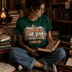 A woman wearing a evergreen Booked & Unavailable cute book graphic t-shirt reading a book in a library.