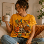 A woman wearing a gold Nature's Nap Team cute animal graphic t-shirt drinking coffee.