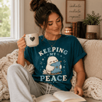 A woman wearing a deep teal Keeping My Peace cute animal graphic t-shirt reading a book.