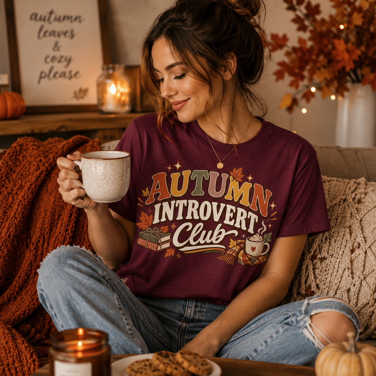 A woman wearing a maroon Autumn Introvert Club cute fall graphic t-shirt enjoying a hot drink.
