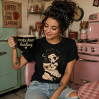 Woman in retro kitchen wearing a black Coffee Clara graphic t-shirt and drinking coffee.
