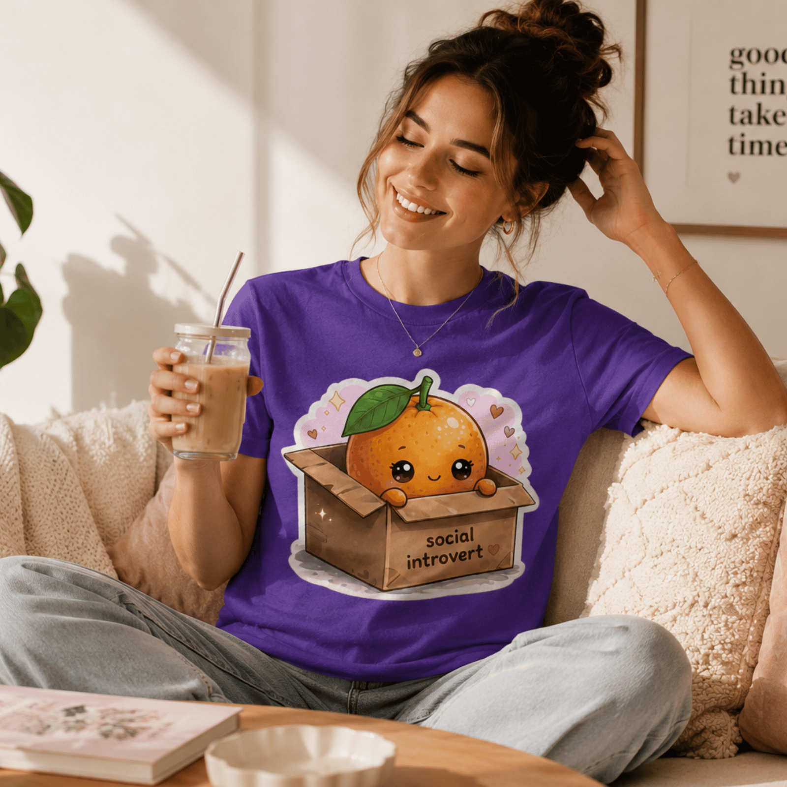 Woman wearing Bowl Goals graphic t-shirt in team purple sitting on couch, drinking an iced coffee.