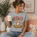 A woman wearing an athletic heather Tiny but Unbothered graphic t-shirt.