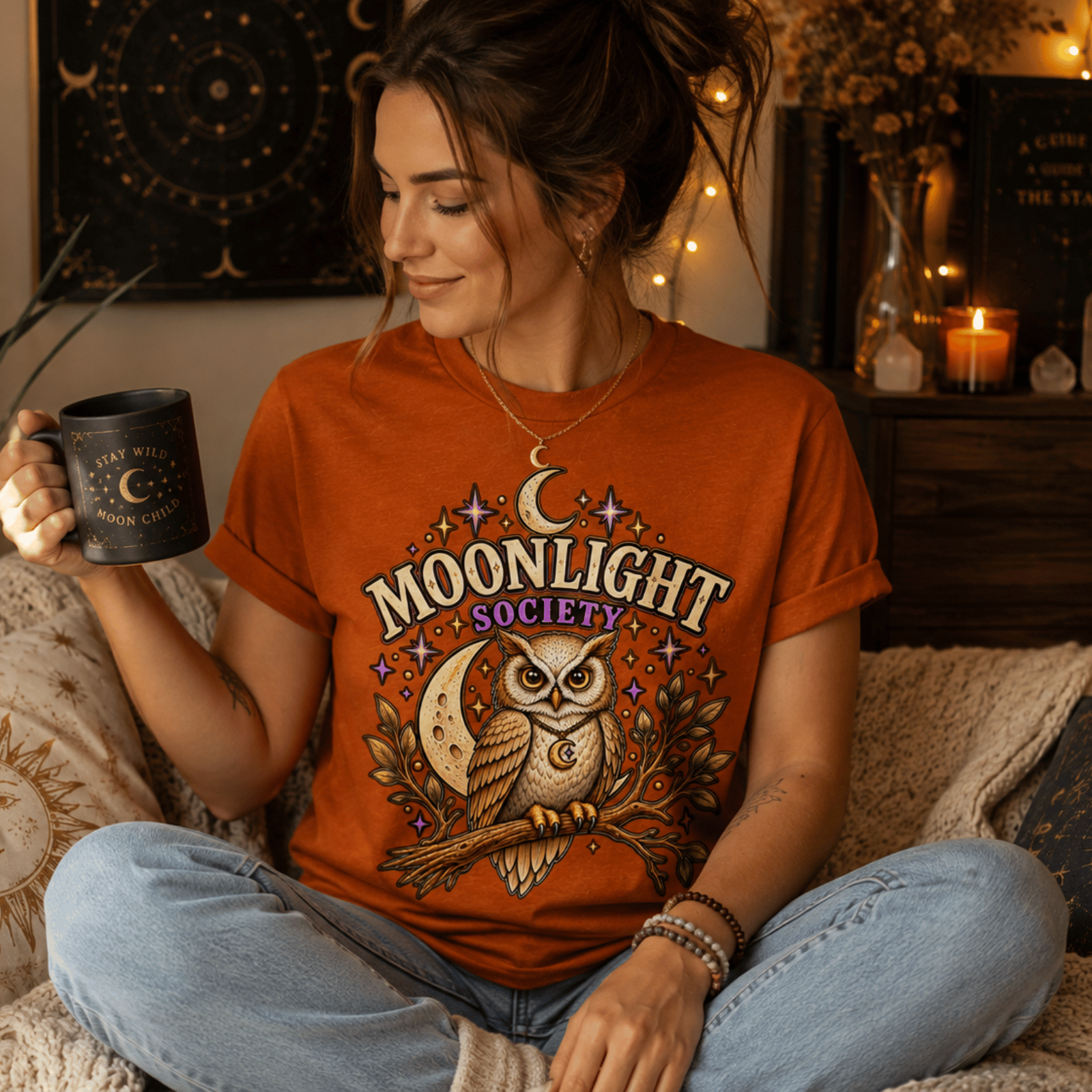 A woman wearing a burnt orange Moonlight Society cute celestial graphic t-shirt drinking coffee.