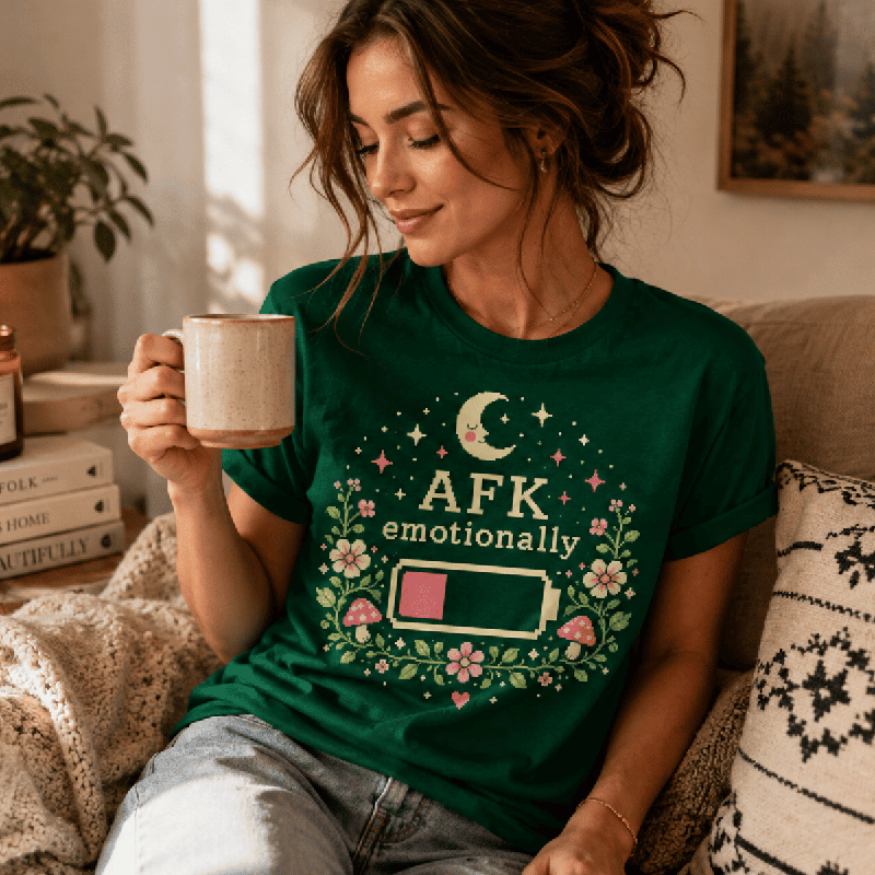 Woman relaxing on a couch wearing the AFK Premium T-Shirt in dark green, holding a mug