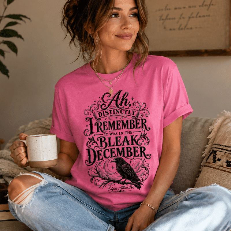 Woman sitting on a couch wearing the Bleak December Premium T-Shirt in charity pink, holding a mug