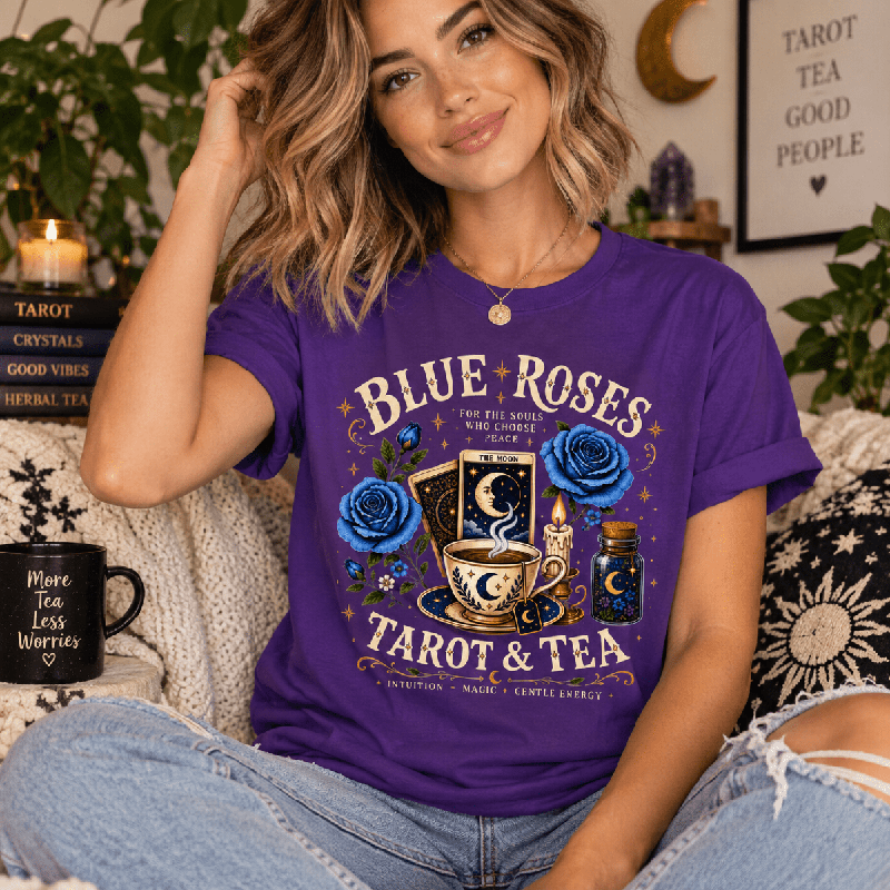 Woman sitting indoors wearing the Blue Roses Premium T-Shirt in team purple, styled with tarot and crystal decor