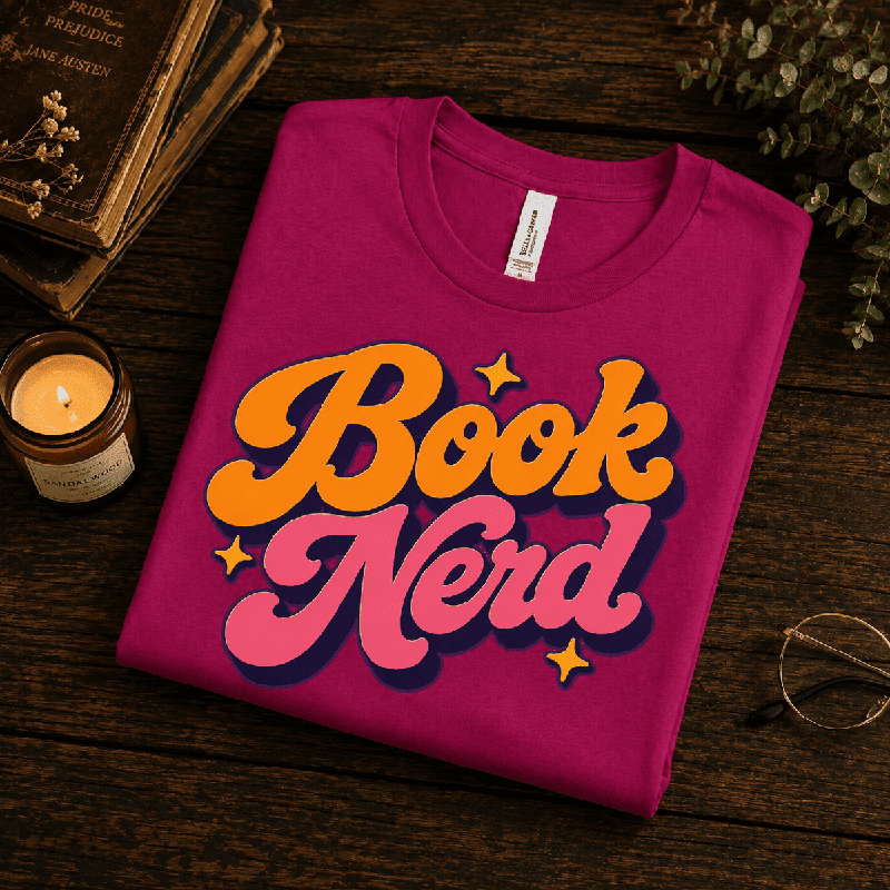 Book Nerd Premium T-Shirt in berry, folded close-up styled with vintage books and a candle