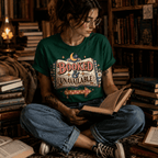 Woman reading on a rug wearing the Booked & Unavailable Premium T-Shirt in evergreen, surrounded by stacked books