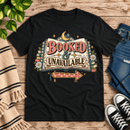 Booked & Unavailable Premium T-Shirt in black, flat lay with open-book and crescent moon graphic