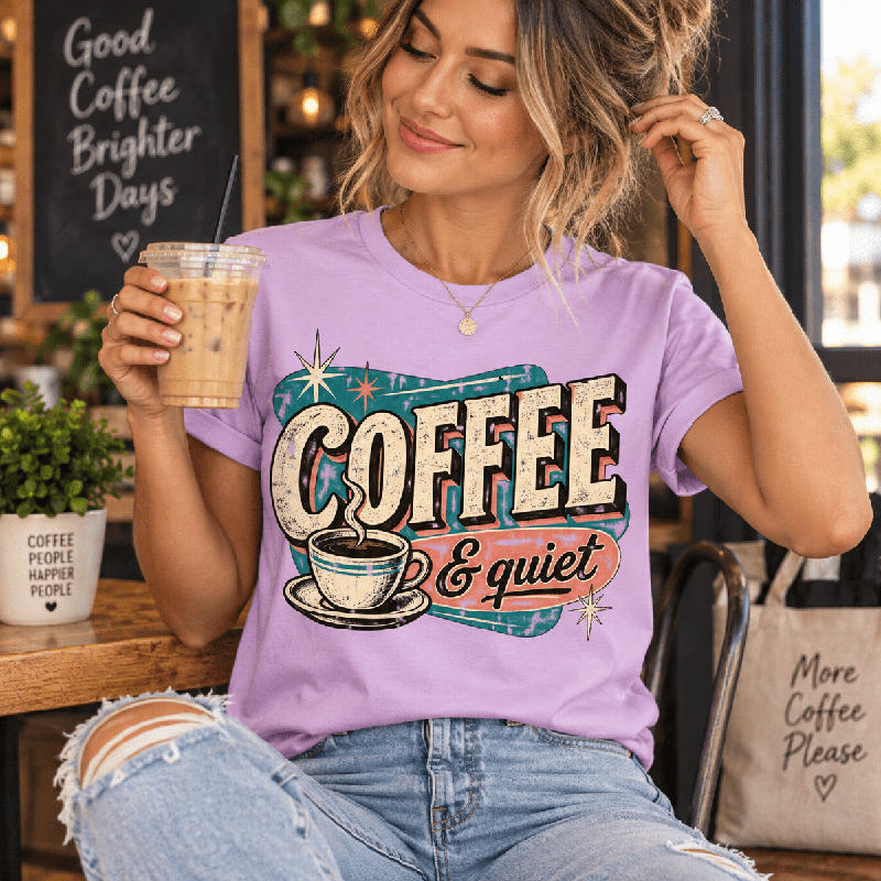 Woman holding an iced coffee in a cafe, wearing the Coffee & Quiet Premium T-Shirt in lilac
